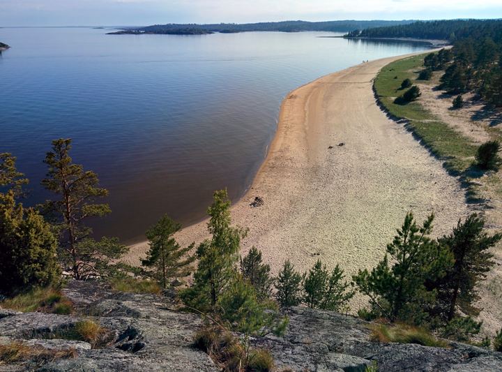 A long sandy beach curving along a calm lake, seen from the cliffs